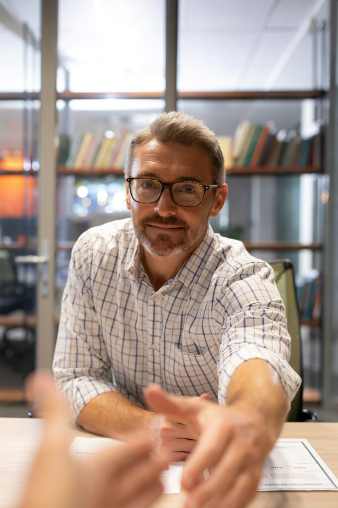 Portrait of confident caucasian businessman shaking hands while sitting with agreement at desk